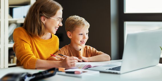 Mutter und Sohn lachend vor Laptop und Arbeitsheft